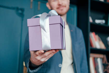 Gift box with gray silver ribbon in the hands of young attracrive man on blue backgroundの写真素材