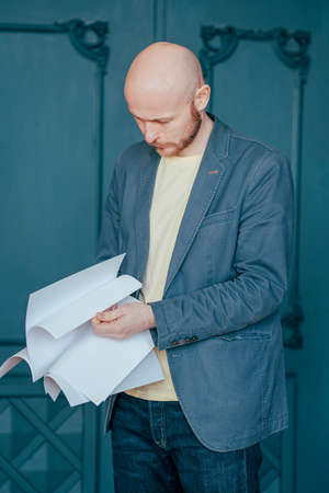 The bald bearded man in blue jacket suit holding sheets of paper in his hands, close upの写真素材