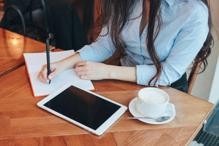 Beautiful charming brunette girl with tablet at table in cafe, student, freelancerの写真素材