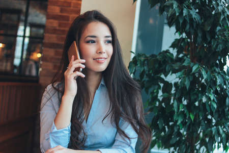 Beautiful charming brunette smiling asian girl talking on smartphone at cafe