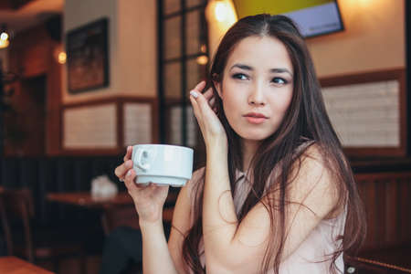 Beautiful charming romantic brunette smiling Asian girl has Breakfast with coffee at cafeの写真素材