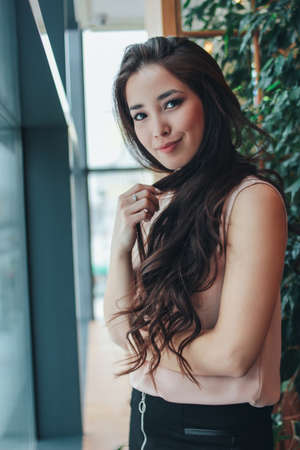 Portrait of beautiful charming romantic brunette long hair smiling asian girl near the window at...