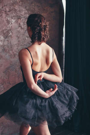 Candid portrait of Ballet dancer ballerina from the back in black dress posing in loft studioの写真素材