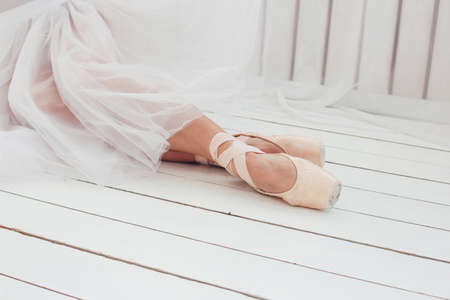 Young woman authentic ballerina ballet dancer in pointe shous sitting on white floorの写真素材