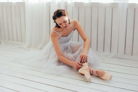 The authentic ballerina ballet dancer sitting on the floor and tying pointe shoesの写真素材