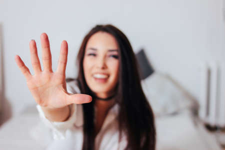 Happy smiling beautiful long hair asian girl young woman pulling hand towards camera sitting on bedの写真素材