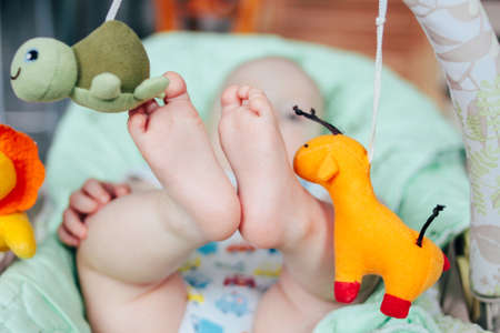 New born feet in woman mother hands in baby seat with bright toysの写真素材