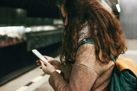 Young woman curly red head girl traveller with backpack using mobile in subwayの写真素材