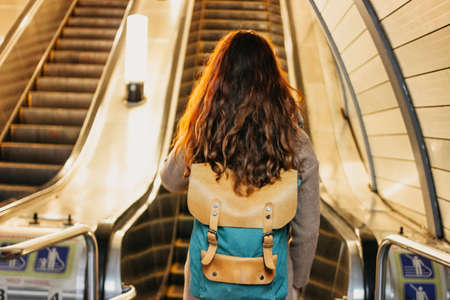 Young woman curly red head girl traveller with backpack and map in subway station in front of escalatorの写真素材