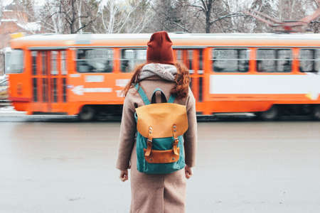 Young woman curly red head girl traveller with backpack in front of tram at the city street