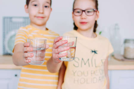 Smiling boy and girl drink clean water at homeの写真素材
