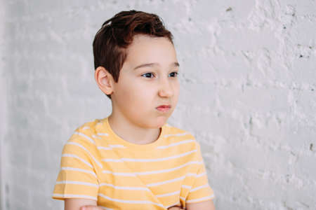 Cute tween angry boy with funny face in yellow t-shirt isolated on white brick wall background