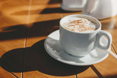 Cup of cappuccino coffee with foam and cinnamon on a wooden table. Hard morning lightの写真素材
