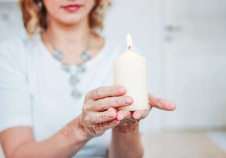 Blonde young woman in white clothing with mehendi holding burning candleの写真素材