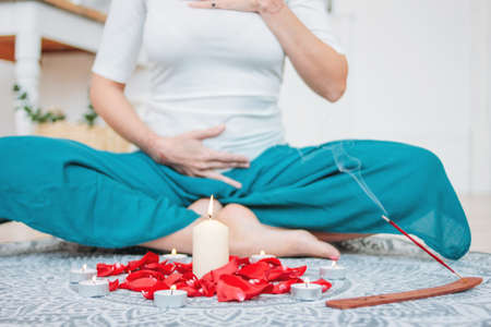 Woman in ethnic costume practicing yoga in front of candles and red rose petals, hands with mehendi on the heart chakraの写真素材