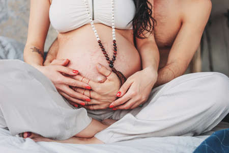Pregnant young woman with long curly hair in ethnic clothes and mala beads with her husband....