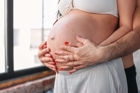 Pregnant young woman with long curly hair in ethnic clothes and mala beads with her husband....