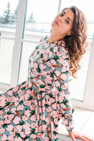 Young charming romantic brunette young woman in summer long dress sitting on window sillの写真素材