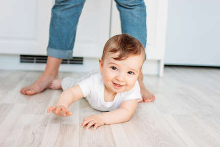 Charming little boy 6 months smiling and looking at the camera on the background of mom's feetの写真素材