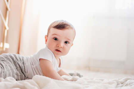 Charming little baby boy 6 months looking at the camera on white blanket in home
