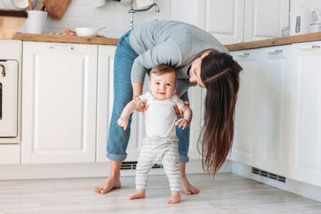 Young mother brunette woman with baby boy in white modern kitchen at home, lifestyle moments