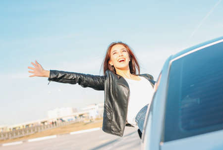 Happpy beautiful charming brunette long hair young asian woman in black leather jacket in car window at sunsetの写真素材