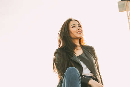 Beautiful charming brunette long hair happy asian girl in black leather jacket at sunset