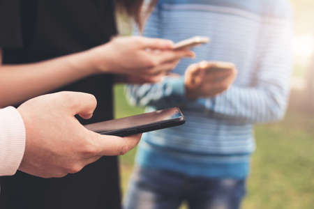 The group of young friends teenagers using mobile at the city street, close up focus on handsの写真素材