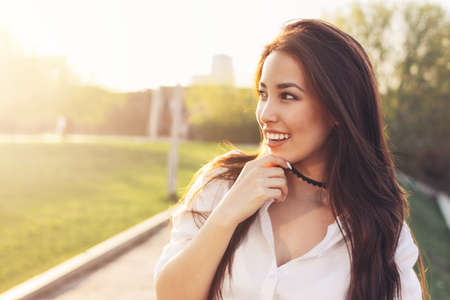 Positive beautiful happy asian girl in white shirt on city street background, summer sunset time