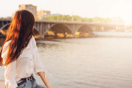 Positive beautiful long hair happy girl in white shirt on city river bridge background, summer...