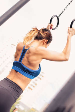 Attractive fit young woman in sport wear girl pulls up on the rings at the street workout area. The...