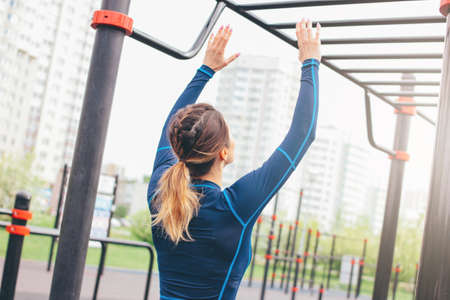 Attractive fit young woman in sport wear girl pulls up on bar at street workout area. The healthy...