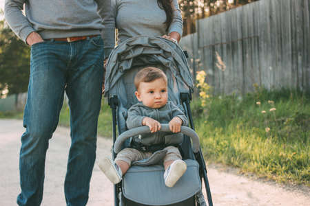 Cute baby boy 8-9 months sitting  in stroller with dad and mom walking on village road outdoors, sensitivity to nature conceptの写真素材