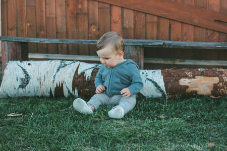 Cute baby boy 8-9 months sitting on grass on the natural wooden wall background outdoors, sensitivity to nature conceptの写真素材