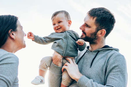 Happy family with cute baby boy on sky background outdoors, sensitivity to nature concept