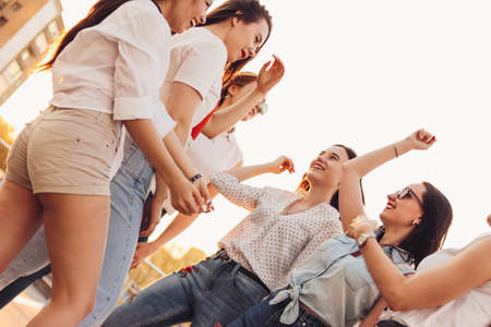 Group of beautiful carefree girlfriends dancing have fun in the city street on background of the evening sunset, summer timeの写真素材