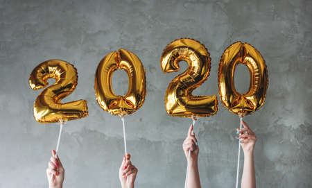 The woman hands holding 2020 numbers balloons on the grey concrete wall background. New Year party...