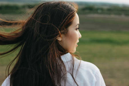 Close up portrait of beautiful carefree long hair girl in white clothes in nature field, view from...