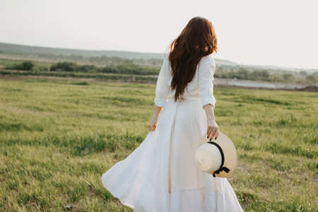 Beautiful carefree long hair girl in white clothes and straw hat enjoys life in the nature field at sunset. Sensitivity to nature conceptの写真素材