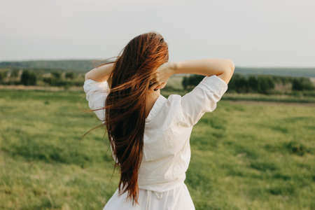 Close up portrait of beautiful carefree long hair girl in the white clothes in field, view from back. Sensitivity to nature conceptの写真素材
