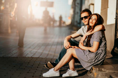 Happy young couple in love teenagers friends dressed in casual style sitting together on the city streetの写真素材
