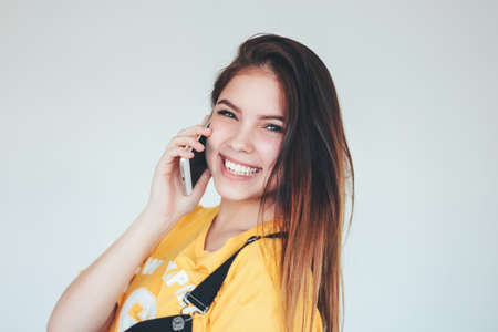 Portrait of happy carefree smiling teenager girl with dark long hair in yellow t-shirt using mobile...