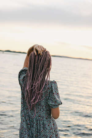 Beautiful romantic young woman with african braids in dress on beach, view from behind, summer...