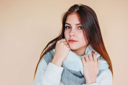 Beautiful smiling girl with clean skin and dark long hair in cozy white sweater and warm scarf on...