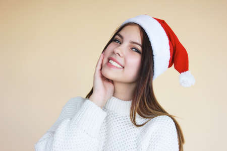 Beautiful smiling girl with clean skin in santa hat an cozy white sweater on the beige backgroundの写真素材