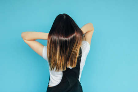 Girl with shiny dark long hair in white t-shirt from behind isolated on the blue backgroundの写真素材