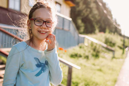 Close up portrait of charming smiling girl in glasses on the background old wooden house cottage, summer time in country sideの写真素材