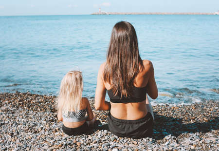 Young fit woman mom with little cute girl sitting on the beach together, healthy lifestyle, sport familyの写真素材