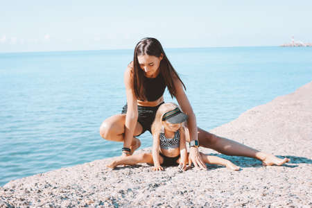 Young fit woman mom with little cute girl exercising on the morning beach together, healthy lifestyle, sport familyの写真素材