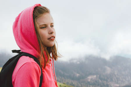 Tween girl with backpack looking on beautiful mountains in the clouds, family travel conceptの写真素材